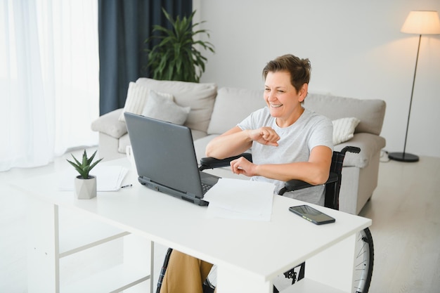 Freelancer in wheelchair using laptop near notebook and papers on table