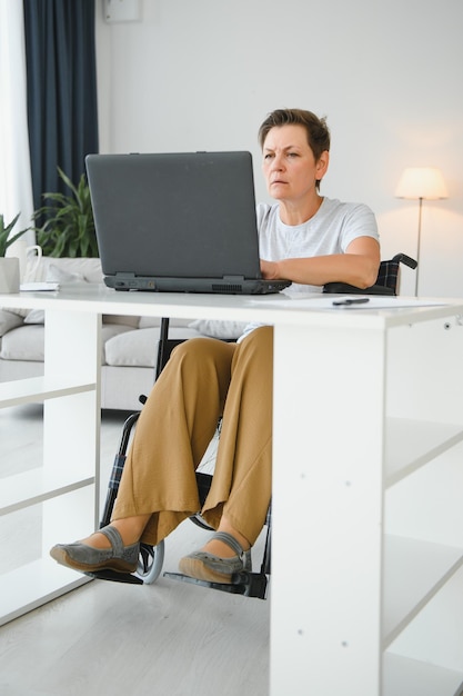 Freelancer in wheelchair using laptop near notebook and papers on table