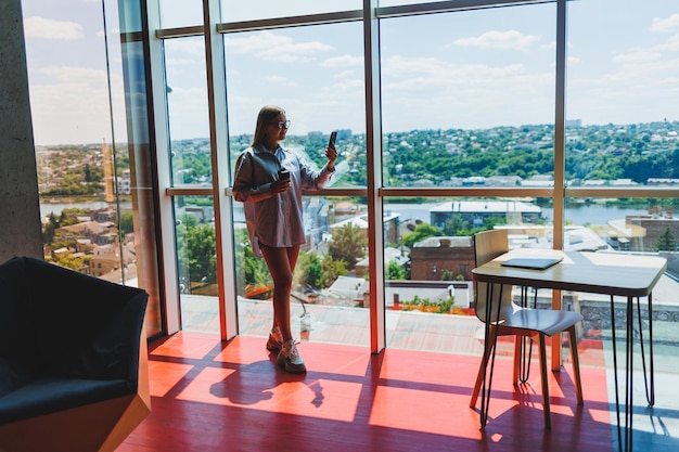 Freelancer woman in classic glasses talking on the phone and smiling while sitting in a modern coworking space carefree millennial woman in glasses enjoying leisure time for communication