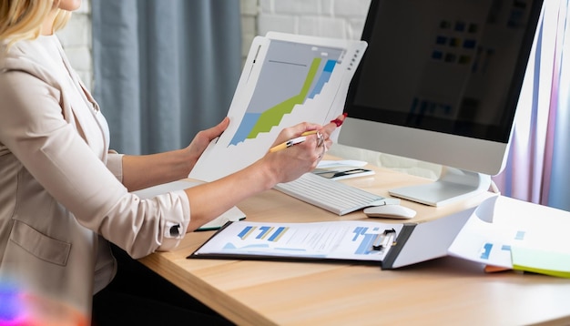 Freelancer woman comparing graphics from clipboard with grafics from computer at business office