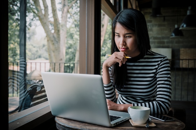 Freelancer woman using her laptop and looking laptop screen while Planning thinking concept in cafe.