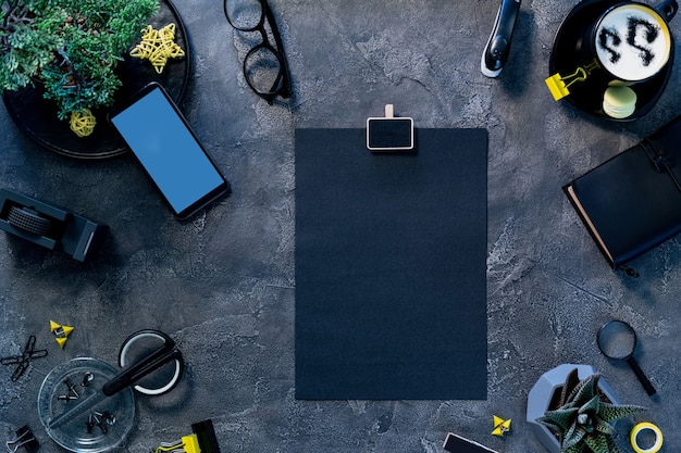 Freelancer workspace flat lay. Paper page attached to clipboard, glowing phone screen on table desk. Workflow process at home office.