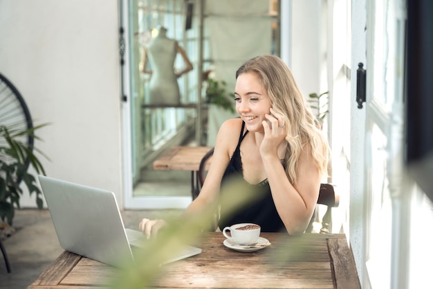 Freeland working girl Sitting in a cafe at a wooden table drinking coffee and using the smartphone on the table as a laptop Young woman surfing the internet chatting blogging