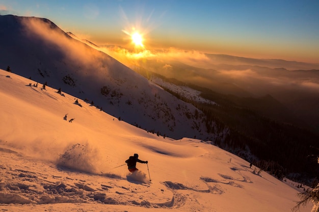 Freeride skier in a beautiful snowy mountains covered with a sunset orange cloudy sky Adrenaline outdoor winter adventures