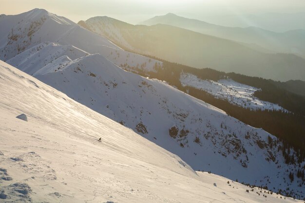 A freerider skier descends a wide slope against the background of mountain ranges and the sunset