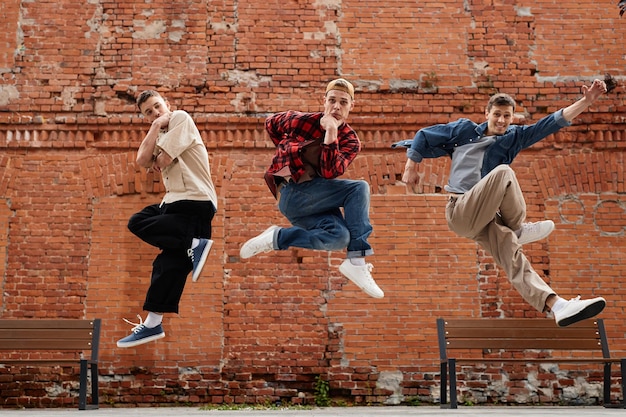 Freeze frame of all male dance team jumping in air and posing against brick wall