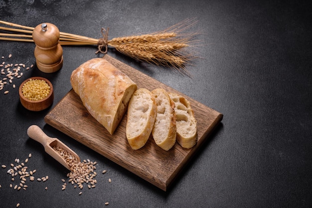 French baguette bread sliced on a wooden cutting board against a dark concrete background