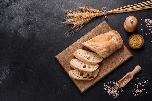 French baguette bread sliced on a wooden cutting board against a dark concrete background