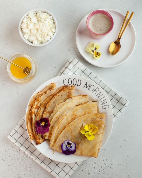 French crepes, pancakes decorated with flowers, a mug of cappuccino and honey. Concept of Breakfast, dessert.