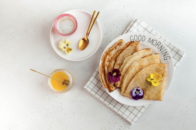 French crepes, pancakes decorated with flowers, a mug of cappuccino and honey. Concept of Breakfast, dessert.