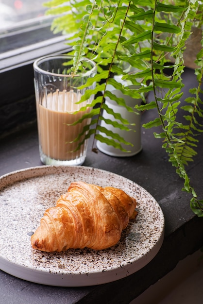 French croissant on a light plate next to a glass of coffee