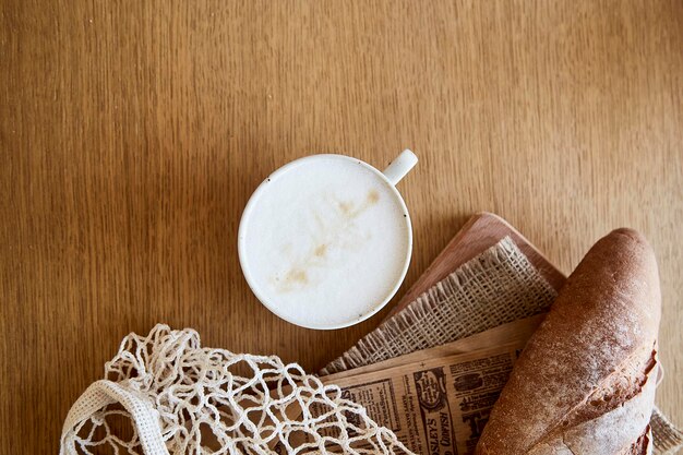 French freshly baked baguette with cappuccino on newspaper on wooden table French traditional morning