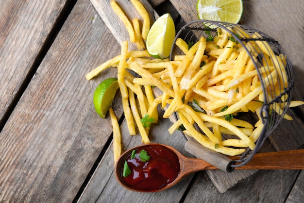 French fried potatoes in metal basket with sauce and lime on cutting board