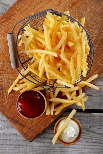 French fried potatoes in metal basket on wooden background