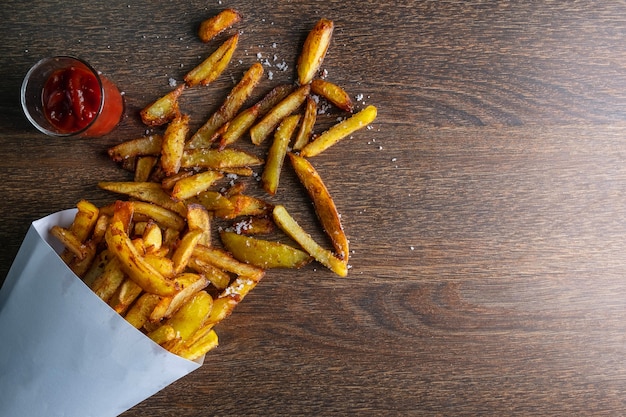 French fries in a paper bag with sauces on wooden back ground