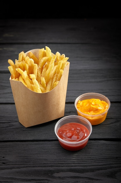 French fries in a paper basket. Fast food.French fries in a paper box with sauce on black background. Copy space