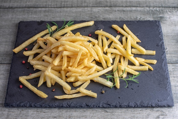 French fries served on black stone plate on gray wooden table