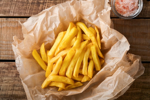 French fries Tasty French fries server on parchment paper on wooden cutting board with tomato and cheese sauce on wooden table background Diverse Keto Dishes Fast food and unhealthy food concept