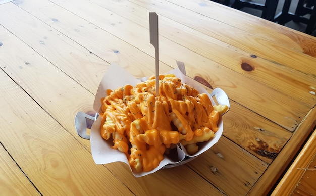 French fries topped with cheese served in a bowl placed on a wooden table