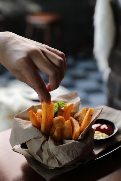 French fries in vintage style on wood background with young woman hand