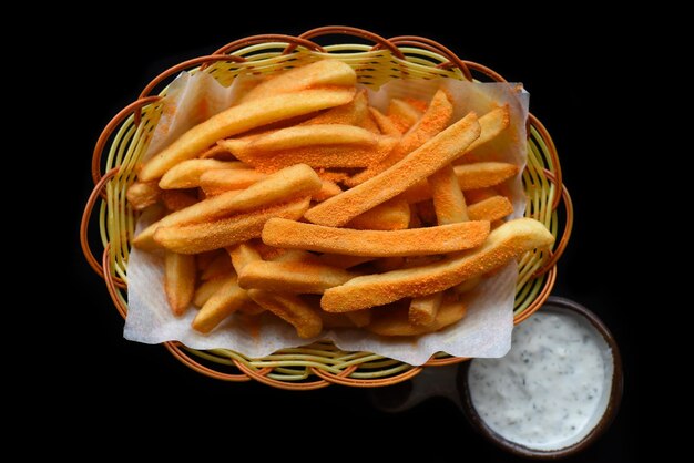 French fries with cheddar cheese in a basket with creamy garlic sauce on black background top view