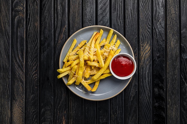 French fries with cheese and ketchup tomato sauce on a plate on dark wooden backdrop