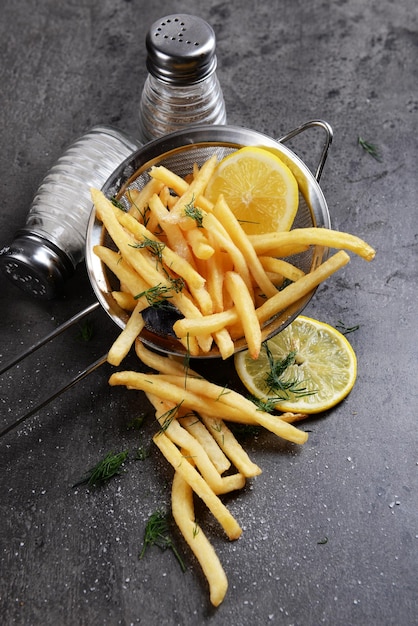 French fries with lemon and salt in sieve on table