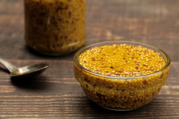 French mustard. Mustard sauce with grains in a glass bowl on a brown wooden stand. close-up