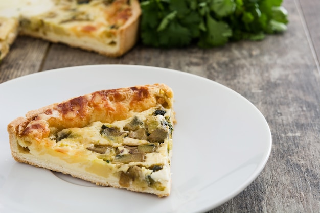 French quiche slice with vegetables on a rustic wooden table