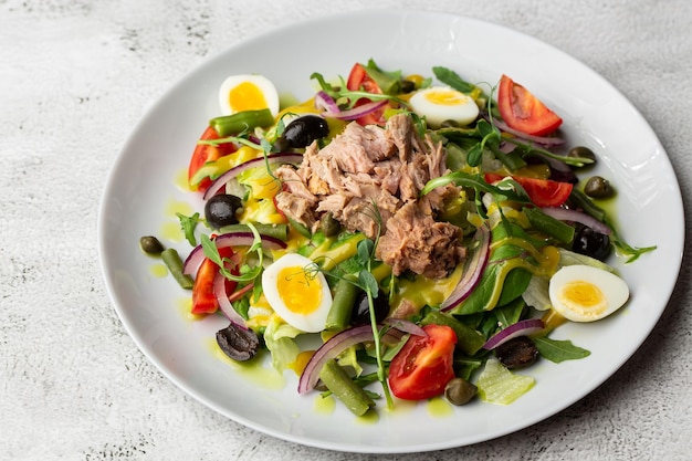 French salad Nicoise with tuna egg green beans tomatoes olives lettuce onions and anchovies on a white background Healthy food