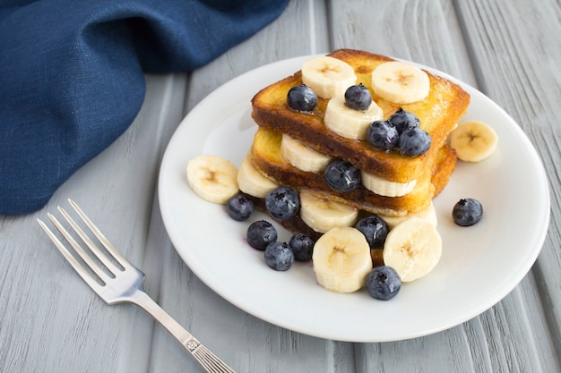 French toasts with blueberries and  banana in the white plate on the  gray surface