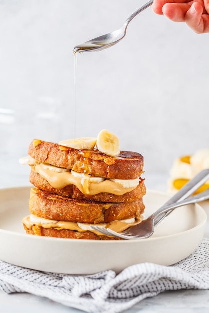 French toasts with peanut butter and banana on a white plate.