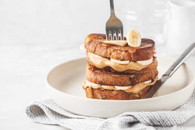 French toasts with peanut butter and banana on a white plate.