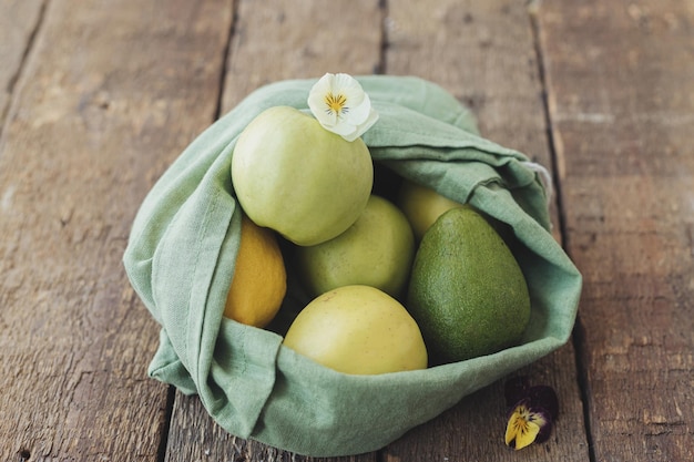 Fresh apples avocado lemons in eco cotton bag with flower on rustic wood Zero waste shopping