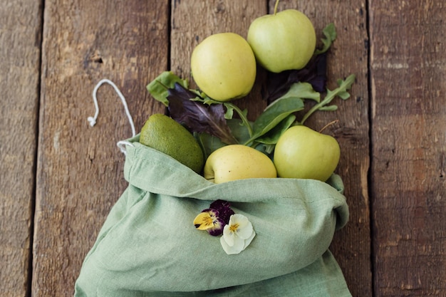 Fresh apples lemon avocado salad leaves in eco cotton bag on rustic wood top view Zero waste