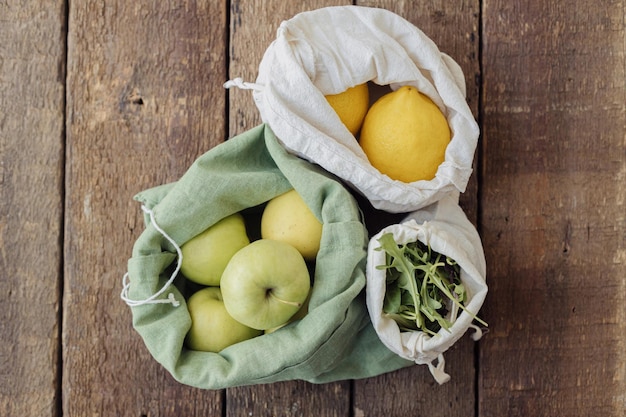 Fresh apples lemons arugula in eco cotton bags on rustic wood Zero waste top view Sustainable