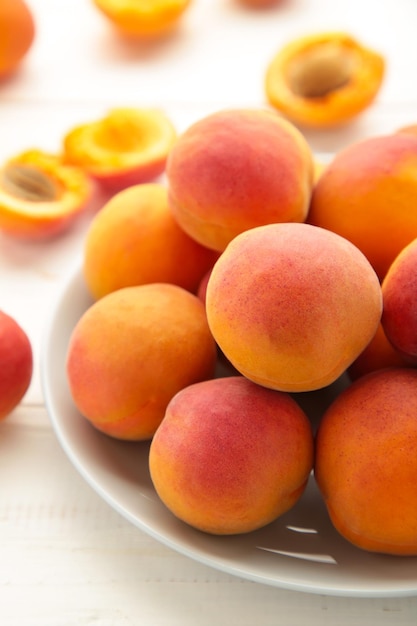 Fresh apricots in the plate on white wooden background Vertical photo