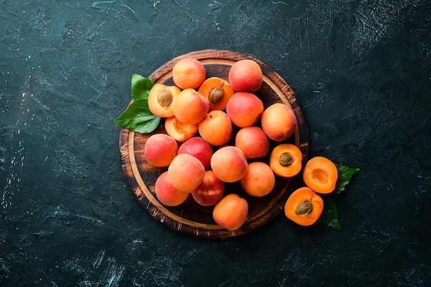 Fresh apricots with green leaves on a black background Rustic style Top view Free space for your text