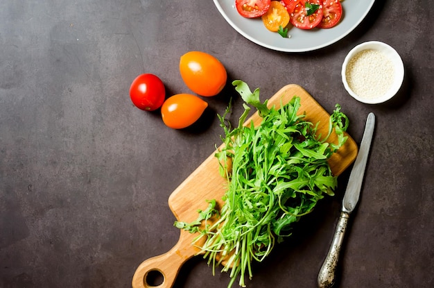 Fresh arugula on cutting board with tomatoes ingredients for cooking