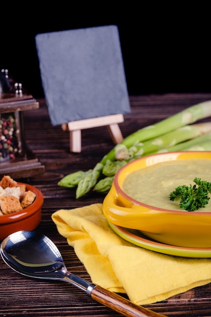 Fresh asparagus creamy soup and ingredients on wooden table, selective focus