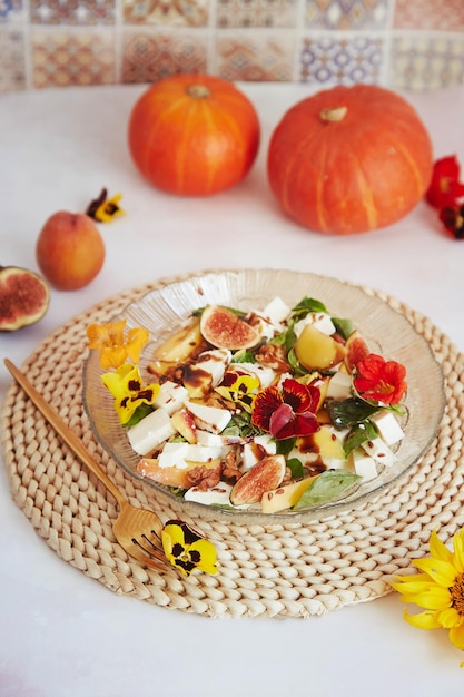 Fresh autumn vegetarian salad with edible flowers figs peach greens and feta on ceramic tile background with fall pumpkin decorations