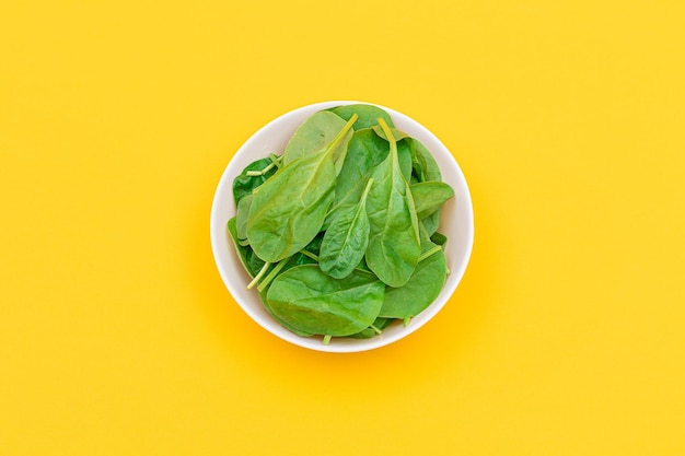 Fresh baby spinach leaves in white bowl on yellow background