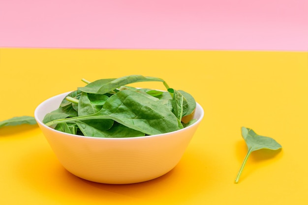 Fresh baby spinach leaves in white bowl on yellow background