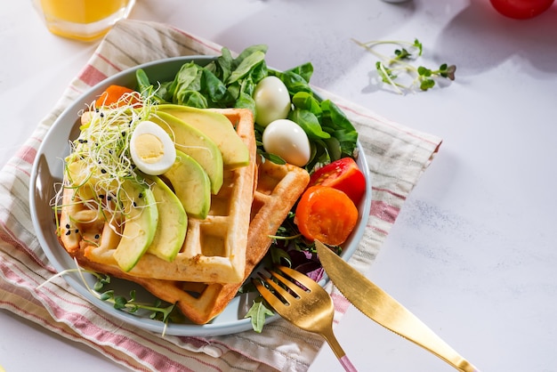 Fresh baked Belgian waffles with spinach, eggs, tomatoes and avocado on blue plate