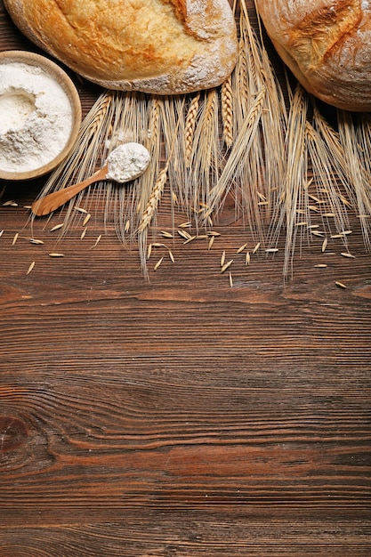 Fresh baked bread a bowl of flour and wheat ears on the wooden background