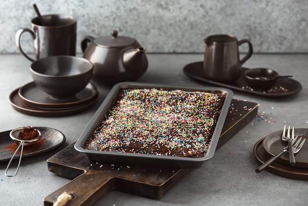 Fresh baked cake covered with dark chocolate icing and colorful sprinkles in a baking pan