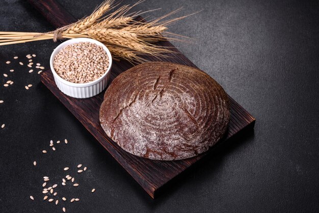 Fresh baked homemade brown bread on a black concrete background with wheat grains