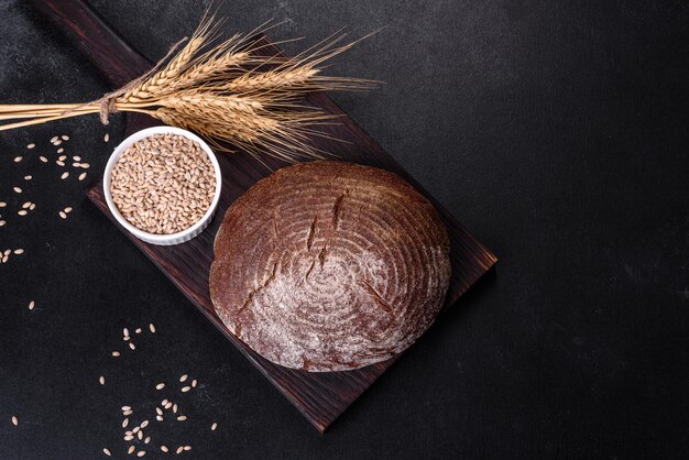 Fresh baked homemade brown bread on a black concrete background with wheat grains