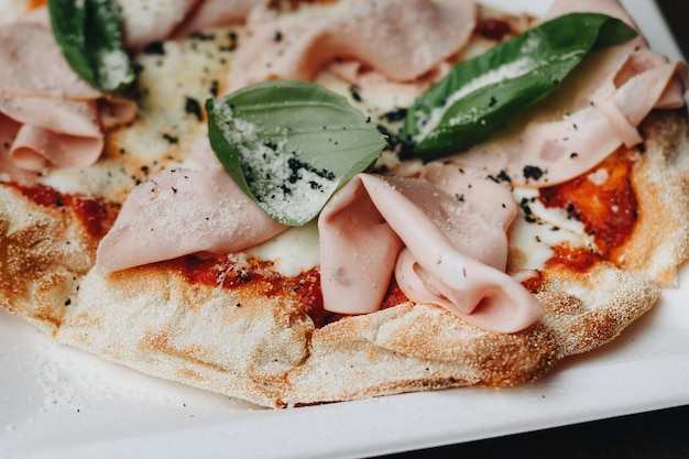 Fresh baked pizza with melted cheese Italian herbs and tomato sauce and fresh basil on a white plate on a kitchen background selective focus