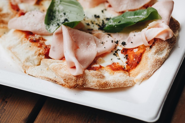 Fresh baked pizza with melted cheese Italian herbs and tomato sauce and fresh basil on a white plate on a kitchen background selective focus